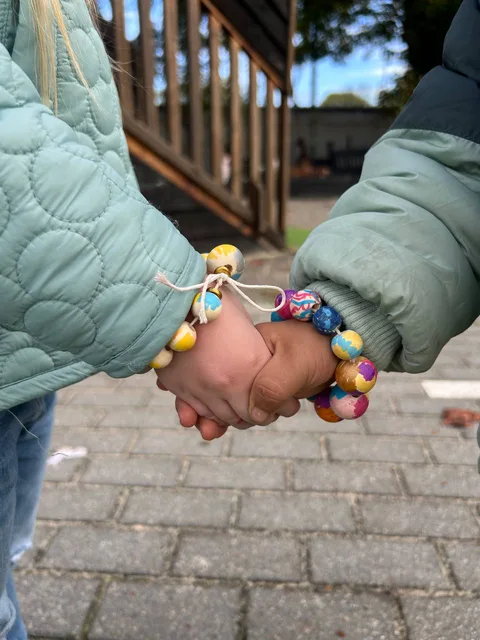 Two young children holding hands wearing colorful handmade bracelets in the courtyard