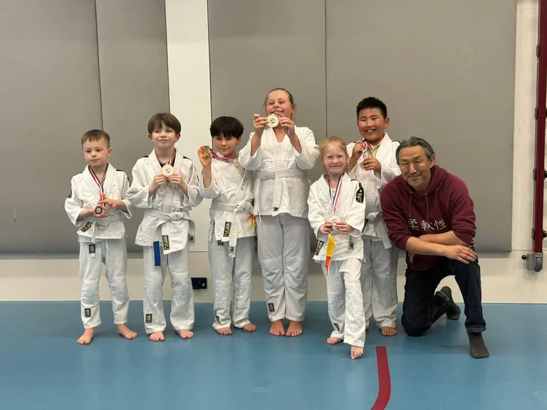 A judo team of students proudly holding medals with their coach